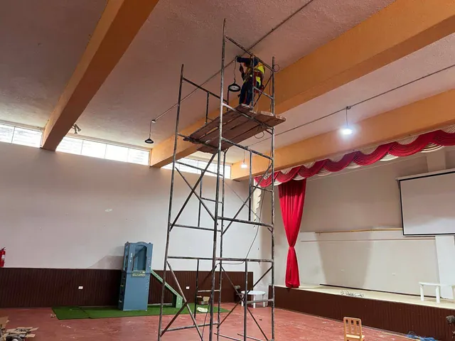 Instalación de luminarias suspendidas en un salón con escenario mediante un andamio