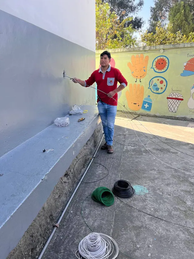 Técnico tendiendo conductores por una canalización en un muro exterior, junto a rollos de cable